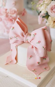 a pink bow cake sitting on top of a white box with flowers in the background