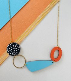 an orange, blue and black necklace with a circle on it hanging from a gold chain