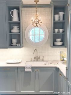 a kitchen with gray cabinets and white counter tops, an oval window above the sink