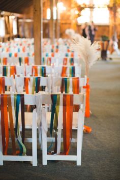 rows of white chairs with colorful ribbons and feathers on the seats are set up for an event