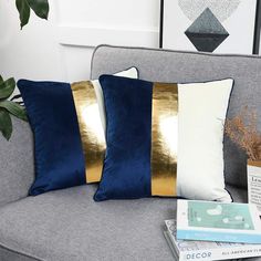 two blue and gold pillows sitting on top of a gray couch next to a plant