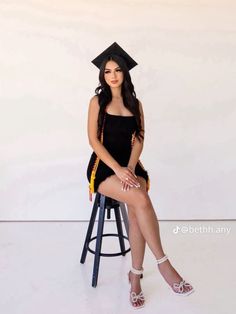 a woman sitting on top of a stool wearing a graduation cap