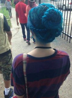 a person with blue hair standing in front of a fence and some people wearing red shirts