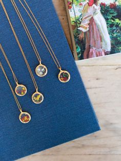 four different necklaces sitting on top of a blue book next to an open book