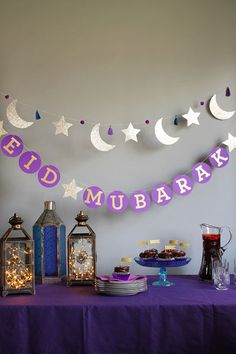 a purple table topped with lots of food next to lanterns and stars hanging from the ceiling