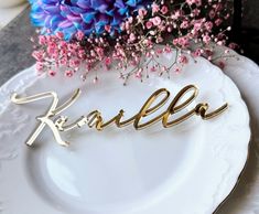 a plate with the word kalleo spelled in gold on it next to purple flowers