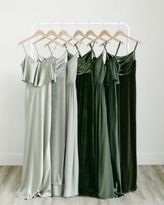 four dresses hanging on a clothes rack in front of a white wall and wooden floor