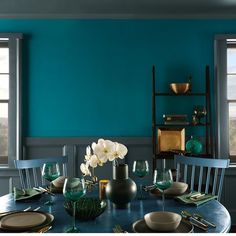 a dining room table set for four with blue walls and white flowers in vases