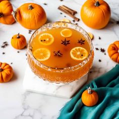 a glass filled with orange juice surrounded by small pumpkins and cinnamon sticks on a marble surface