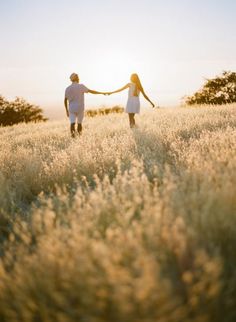 two people holding hands while walking through a field