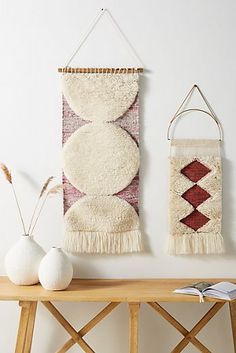 two wall hangings on a white wall next to a wooden table with vases