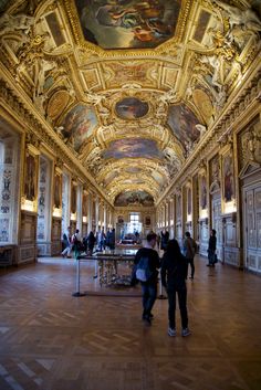 people are standing in an ornate hall with paintings on the ceiling