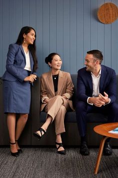 three people sitting on a couch talking to each other in an office setting with blue walls and wood paneling