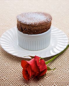 a single red rose sitting on top of a white plate next to a chocolate cake