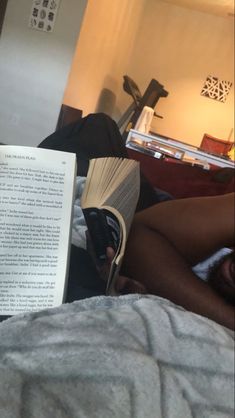 an open book laying on top of a bed next to a person with no pants