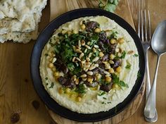 a black plate topped with hummus and vegetables next to silverware on a wooden table