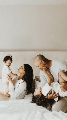 a family laying in bed together and smiling at each other while the child is holding his mother's head