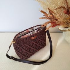 a crocheted brown purse sitting on top of a table next to a vase