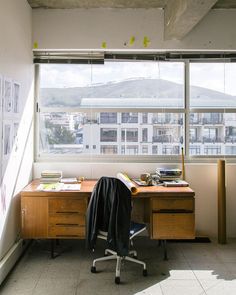 an office with a desk and chair in front of a large window overlooking the city