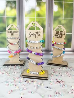 three wooden christmas trees with beaded bracelets in front of a window and confetti sprinkles scattered around them