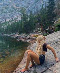 a woman sitting on top of a rock next to a lake