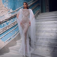 a woman in a white dress standing on some steps with a veil over her head