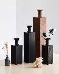 several black vases are lined up on a table with flowers in the middle and one is empty