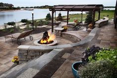 an outdoor fire pit with benches and chairs around it, near the water's edge