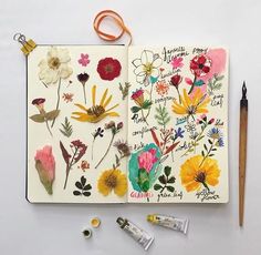 an open notebook with flowers on it next to markers and pencils, along with two pens