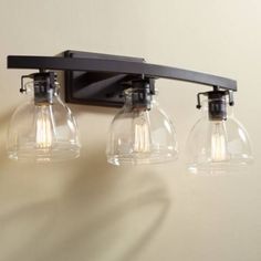 three light fixture mounted on the wall with clear glass shades and black metal frame,