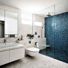 a modern bathroom with blue and white tiles on the shower wall, toilet and sink