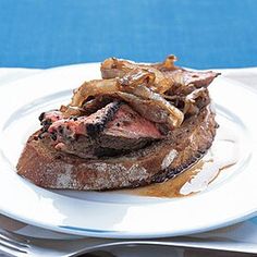 a white plate topped with meat covered in gravy next to silverware on a blue table cloth