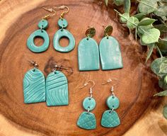 six pairs of earrings on top of a wooden table next to green leaves and greenery