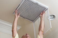 a man is working on an air conditioner in his home with one hand up to the ceiling