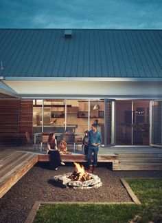 three people standing around a fire pit in front of a house