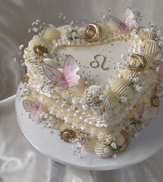 a heart shaped cake decorated with flowers and butterflies on a white tableclothed surface