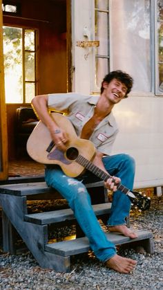 a man sitting on steps holding an acoustic guitar and smiling at the camera with his right hand