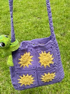 a purple crocheted bag with sunflowers on it sitting in the grass