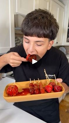 a young boy eating strawberries with toothpicks in a paper tray on a kitchen counter