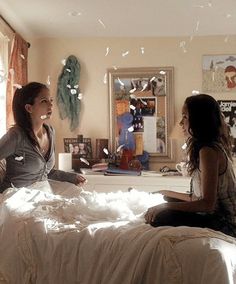 two women sitting on a bed in a room with confetti falling from the ceiling