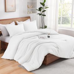 a bed with white comforters and pillows in a room next to a potted plant