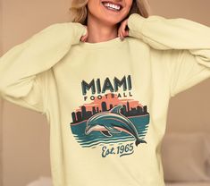 a woman is smiling and holding her hands on her head while wearing a miami football sweatshirt