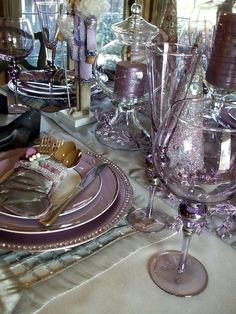 the table is set with purple glassware and silver plates, napkins and candles