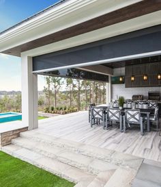 an outdoor kitchen and dining area with pool in the backgrouund, overlooking trees