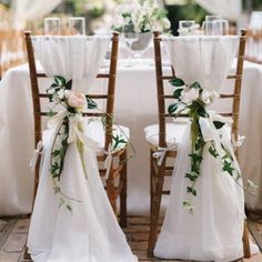 two wooden chairs with white sashes and flowers tied to them, sitting on top of each other