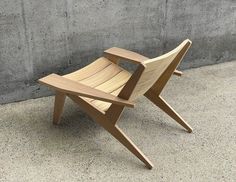 a wooden chair sitting in front of a cement wall on concrete flooring next to a building