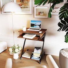 a laptop computer sitting on top of a wooden desk next to a white chair and potted plant