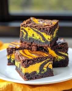 some brownies with yellow and black swirls on a white plate next to a window