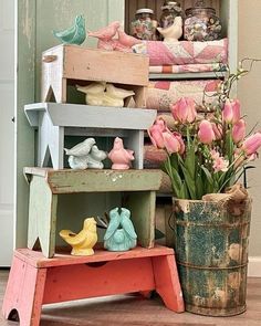 some pink tulips are sitting in front of an old wooden shelf with other small figurines on it