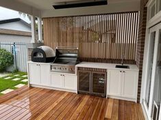 an outdoor kitchen with wood flooring and white cabinetry on the outside side of the house